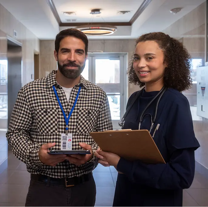 Two people standing together with clipboards smiling at camera