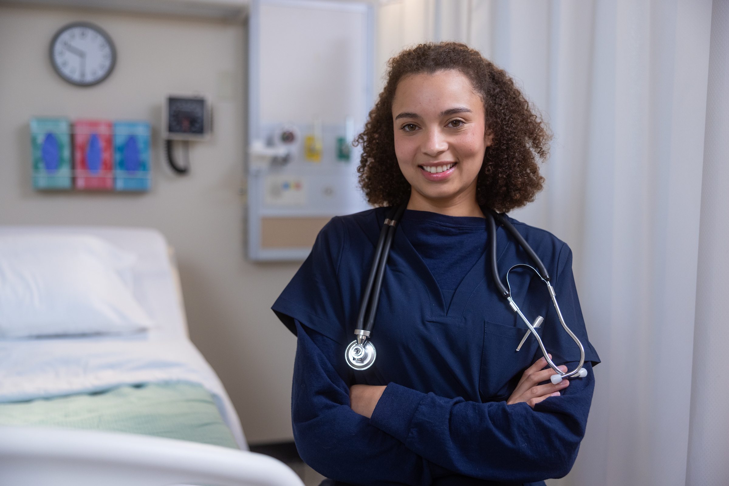 Nurse standing next to a hospital bed wearing scrubs and a stethoscope.