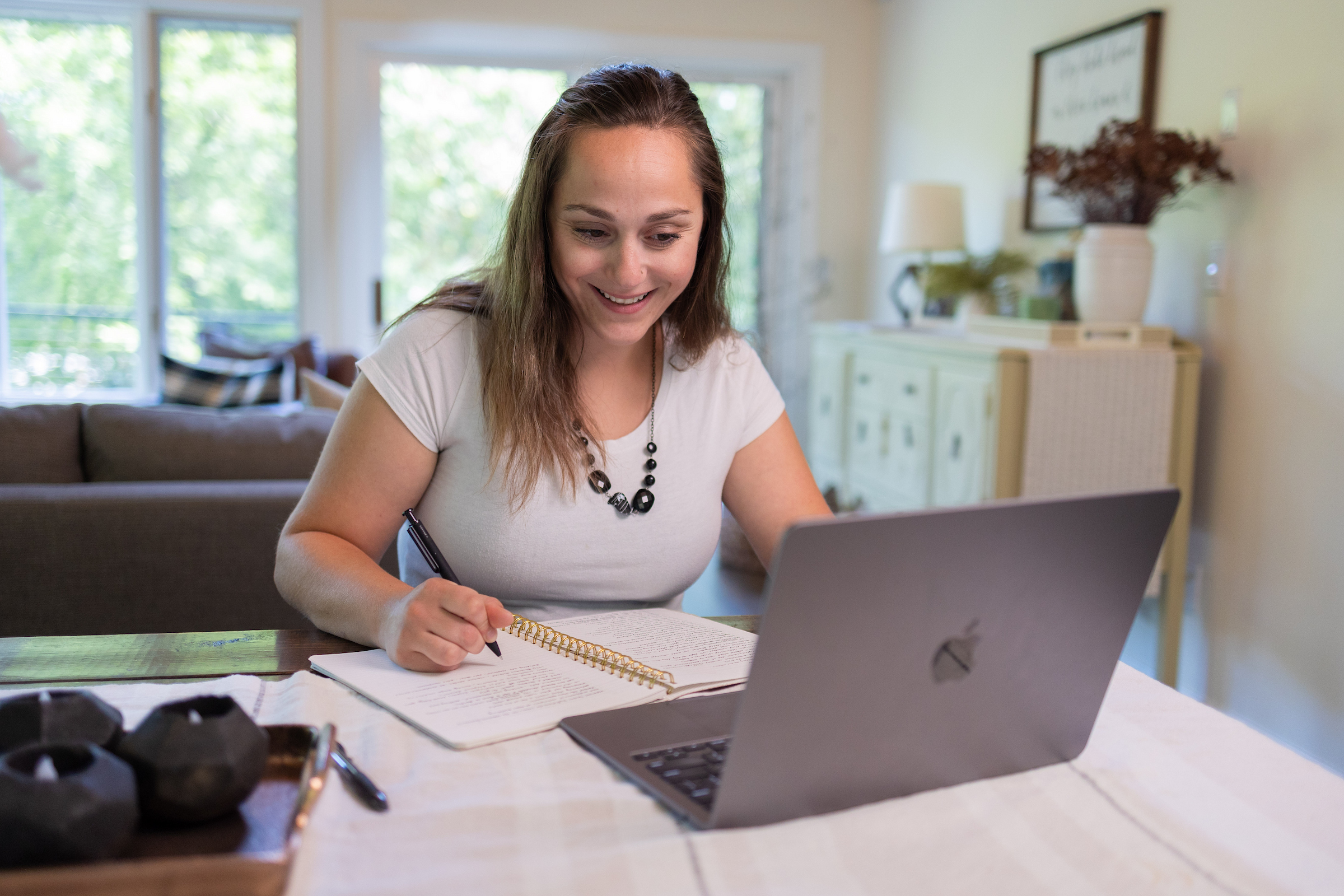 Student sitting at a desk using a laptop and writing in a notebook.