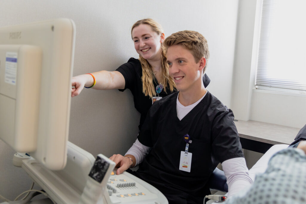 Two diagnostic medical sonography students looking at a monitor in a simulation setting.