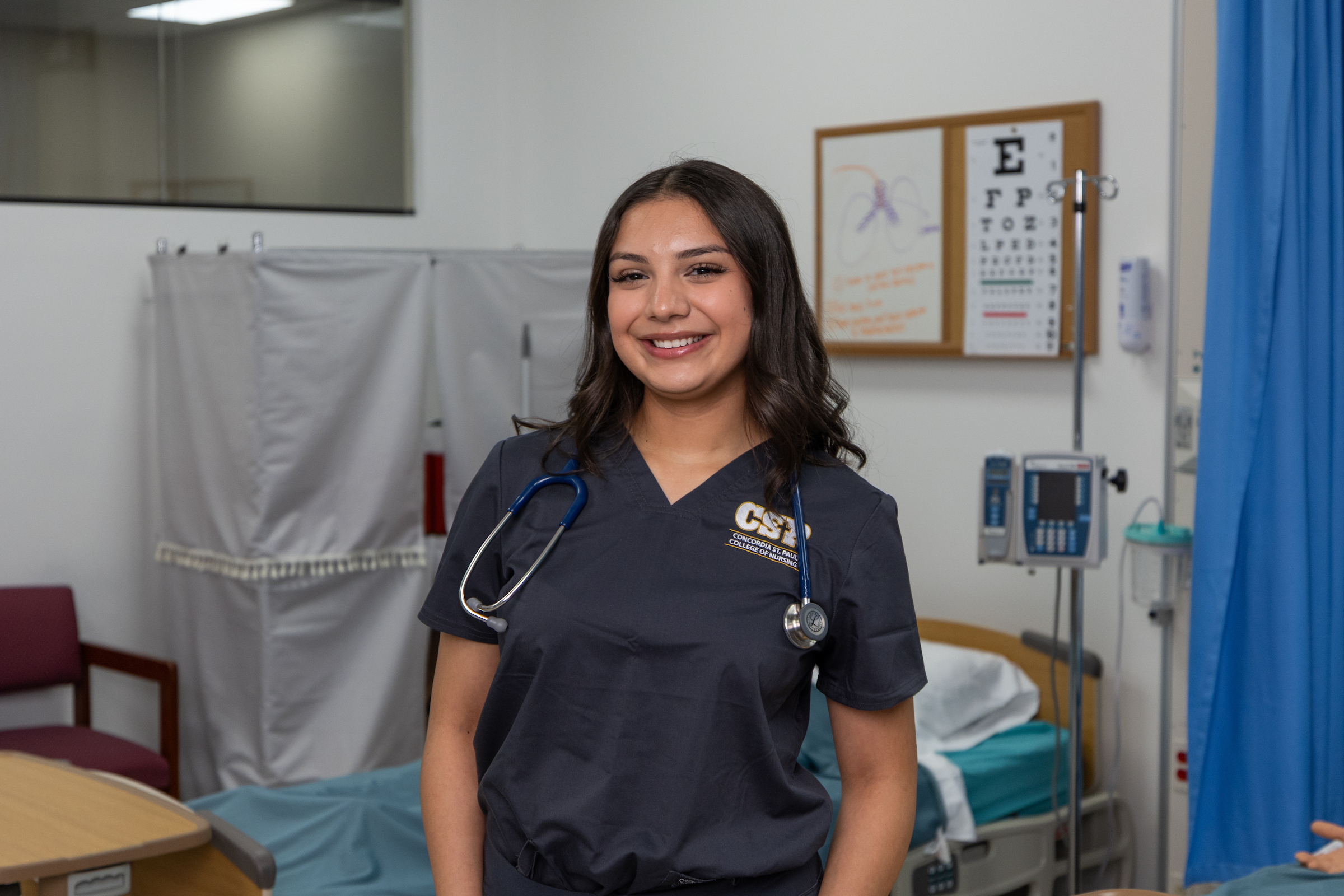 Nursing student standing in a lab setting wearing scrubs and a stethoscrope.