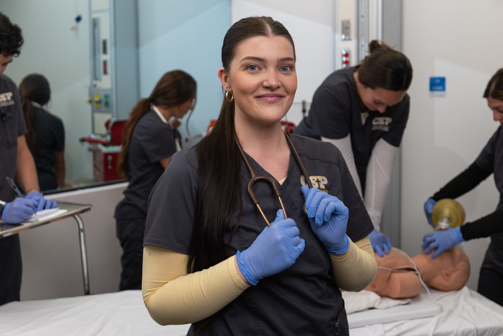 Nursing student wearing a stethoscope standing in a classroom setting.