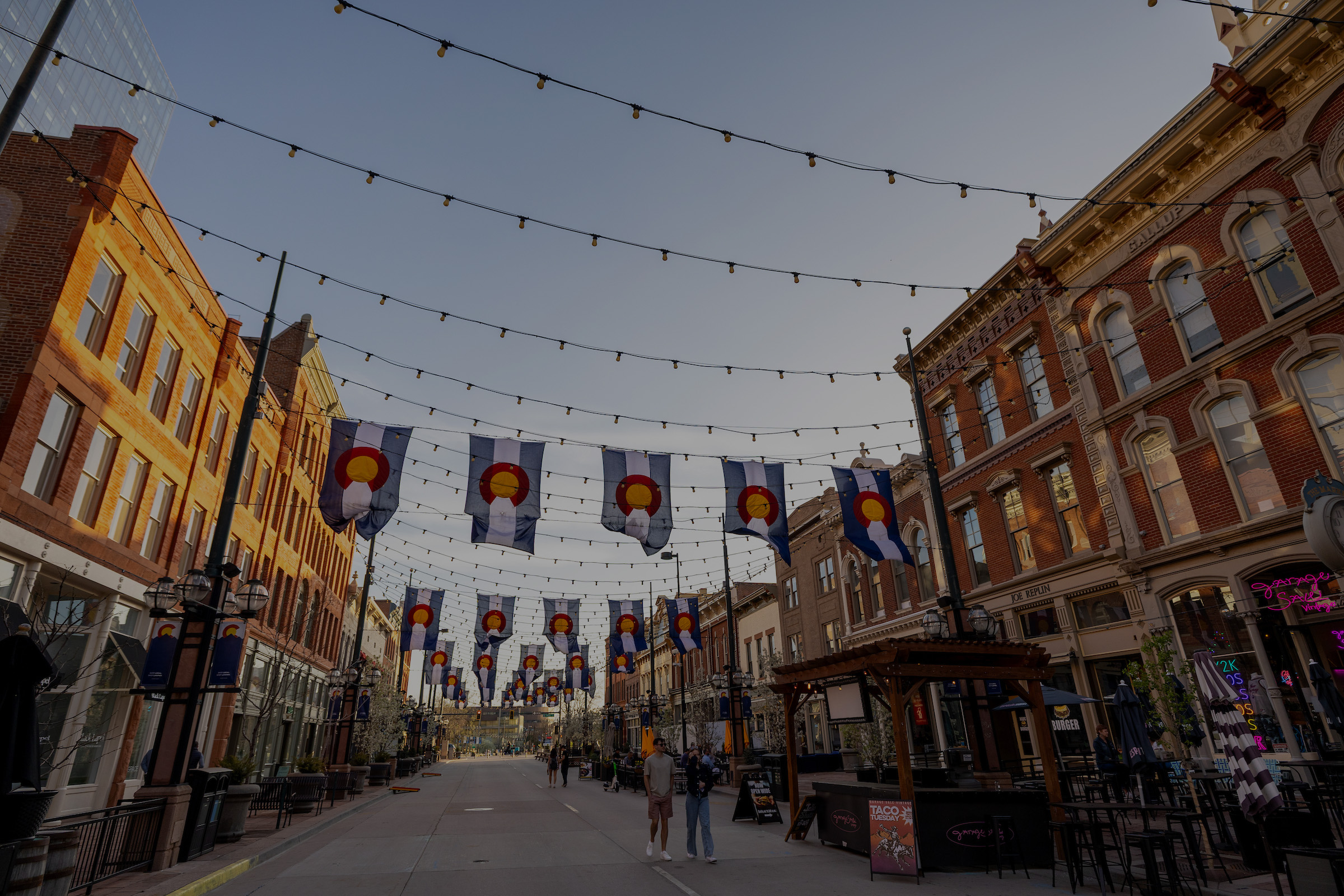 Downtown Denver with lights and Colorado state flags draped between buildings on both sides of the street.