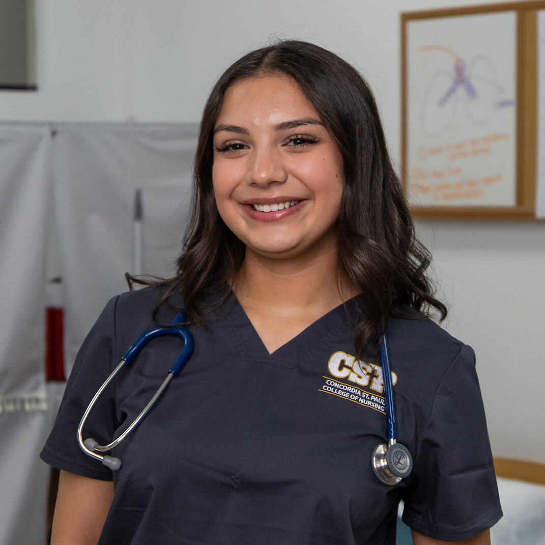 ABSN student wearing scrubs and stethoscope in a lab setting.