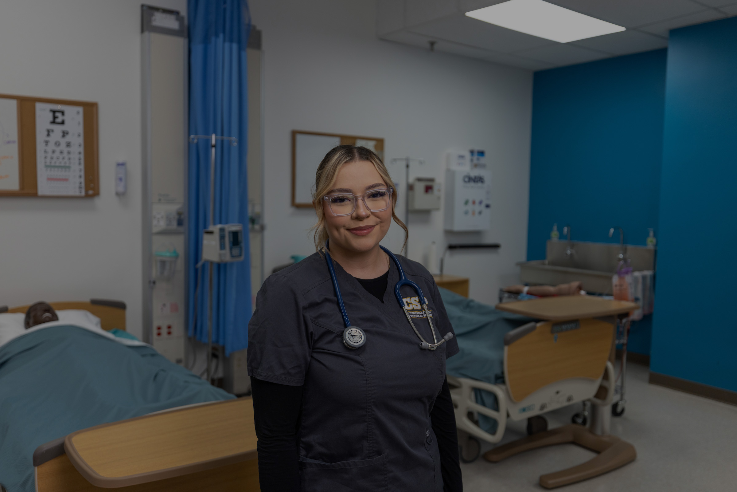 Nursing student wearing scrubs standing in a nursing lab.