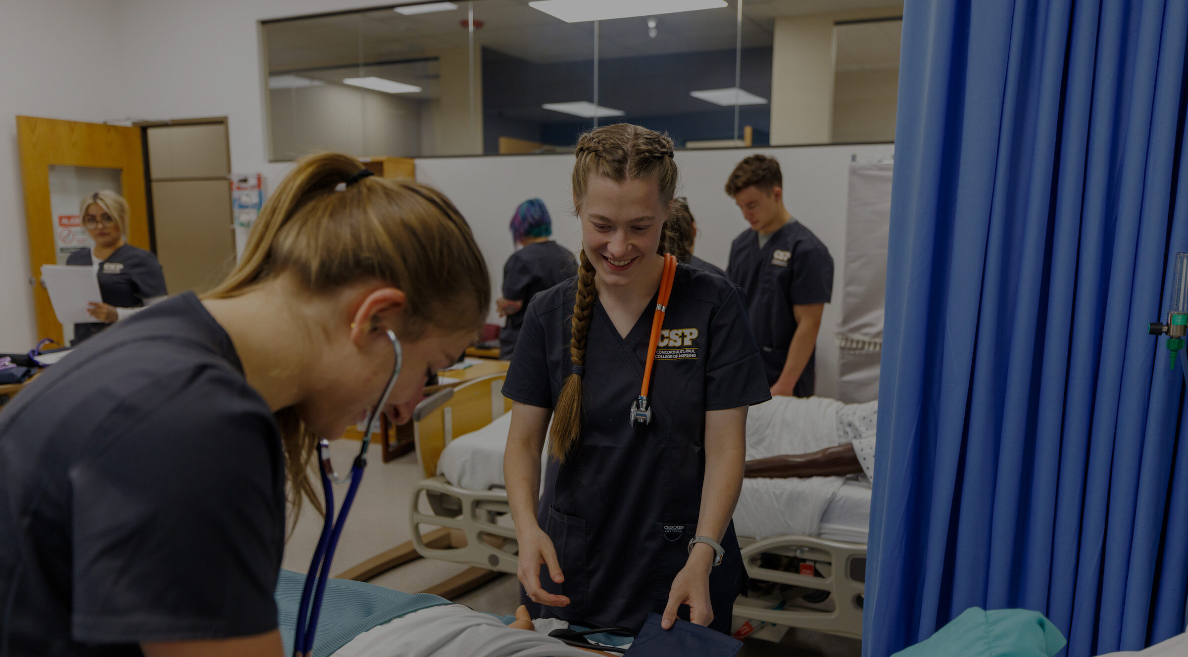 Two nursing students wearing stethoscopes in a learning lab setting.